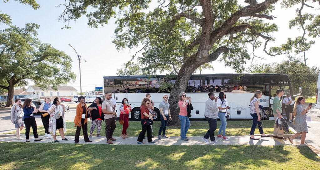 Line of people on a sidewalk in front of a shuttle bus.